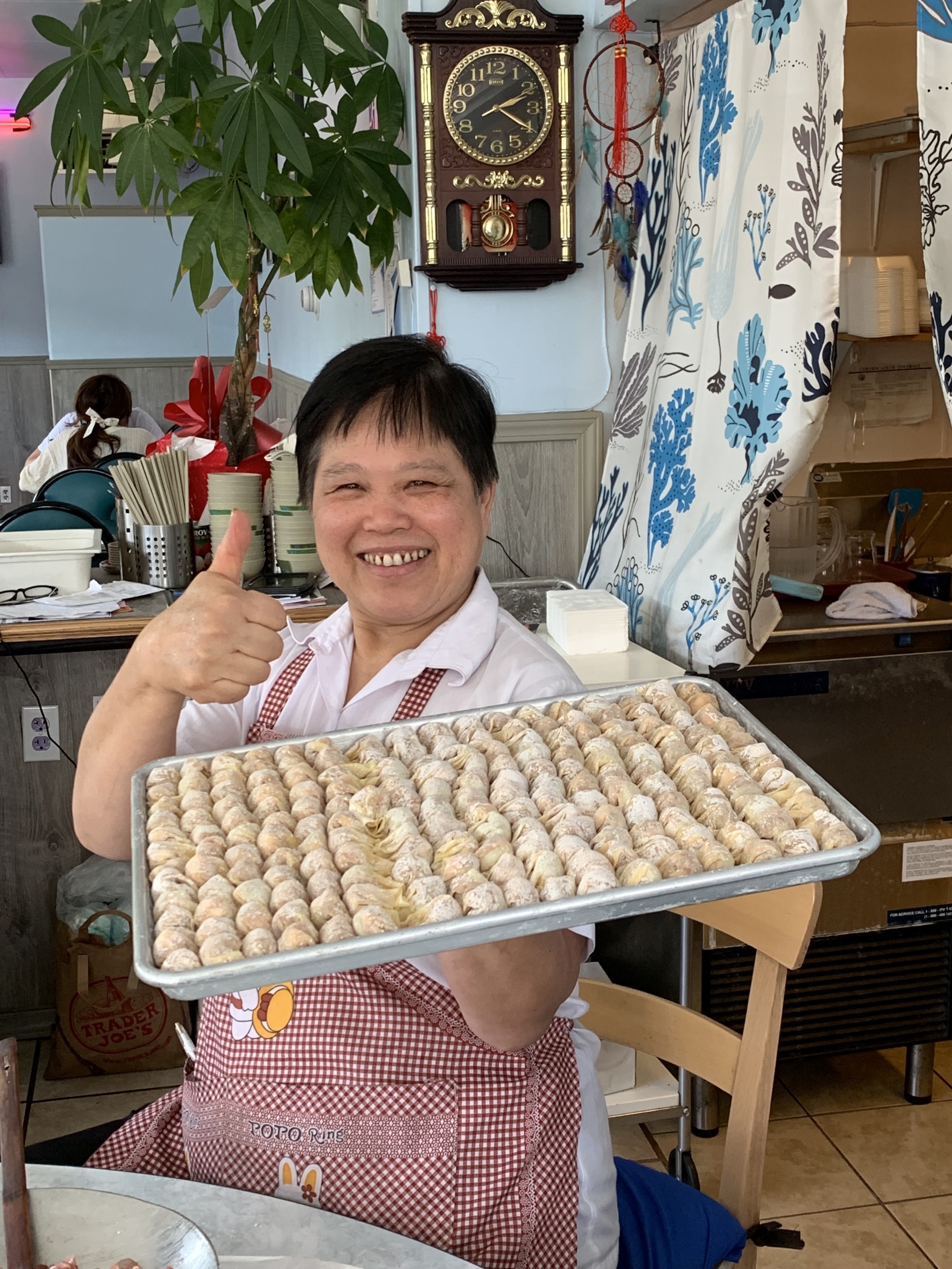 Owner Qiping Ng holds a tray of freshly made wontons and gives the thumbs up sign.