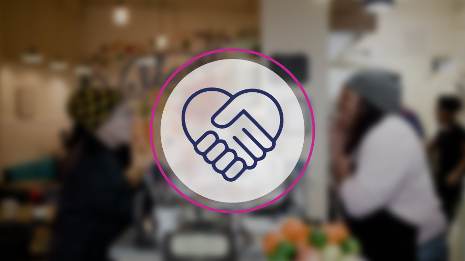 Clasped hands icon in front of a blurred background scene in a cafe.