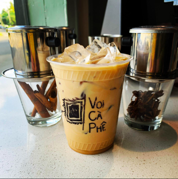 An iced latte sits between two phin coffee makers sitting over glasses of cinnamon and star anise