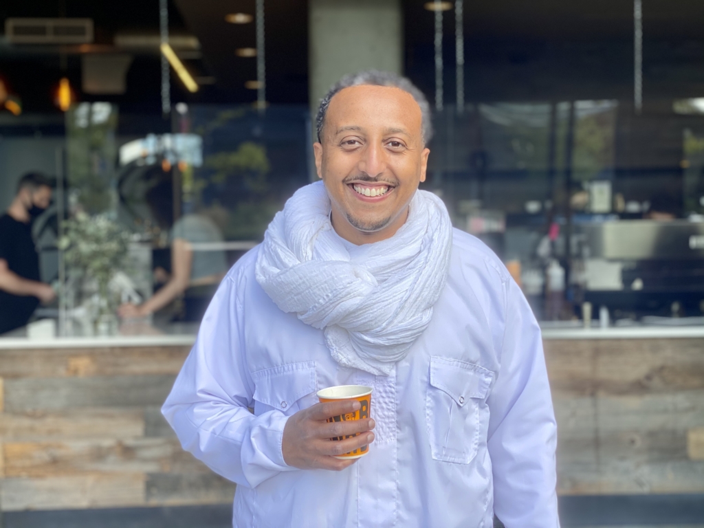 Boon Boona owner, Efrem Fesaha standing in his coffee shop holding a cup of coffee.