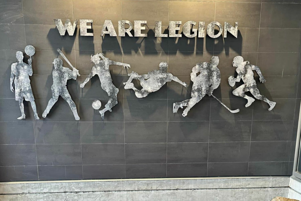 photo of metal wall art at Legion Sports Bar that reads "We Are Legion" with metal cutouts of people playing different sports.