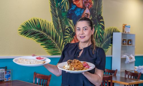 Caribe Latin Cuisine owner holding two plates of food